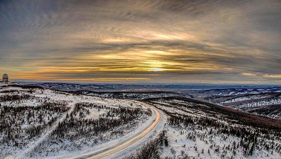 The sun rising over a winding road and white snow-covered hills in Fairbanks, Alaska.