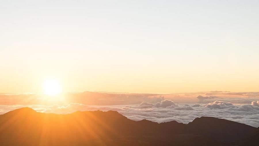 The sun rising over Haleakala National Park, with rays of sunlight shining through clouds over a beautiful mountain scape.